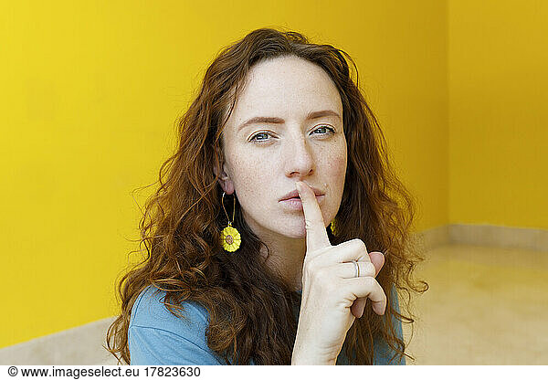 Woman with finger on lips in front of yellow wall at home