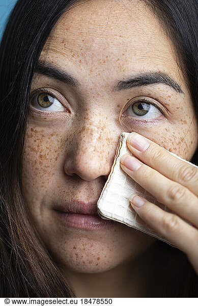 Woman with freckles cleaning face with makeup wipe