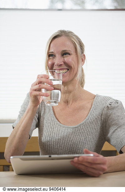 Woman with glass of water and digital tablet  smiling