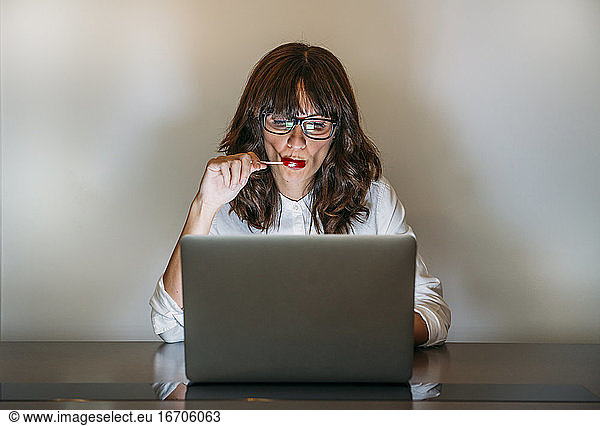 Woman with glasses works with computer and eats a candy