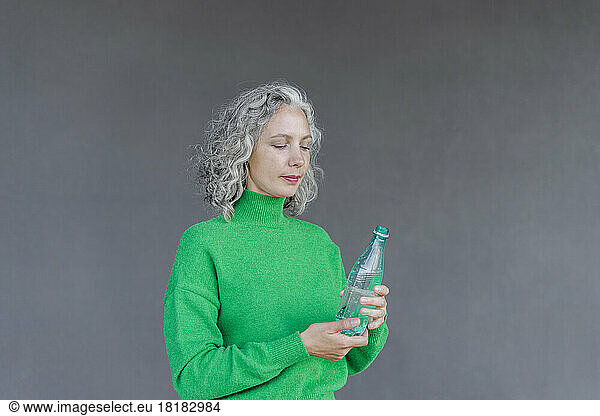 Woman with gray hair holding green water bottle in front of wall