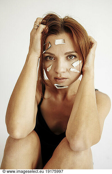 Woman with hand in hair and broken mirror pieces on face