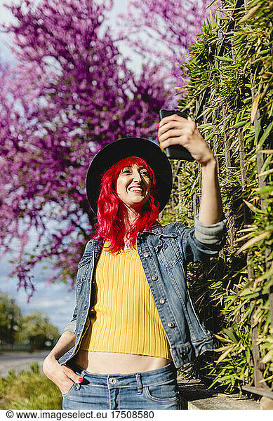 Woman with hand in pocket taking selfie through smart phone on sunny day
