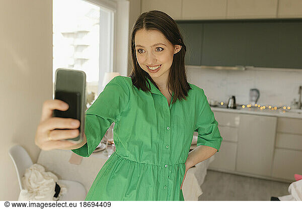 Woman with hand on hip taking selfie through smart phone at home