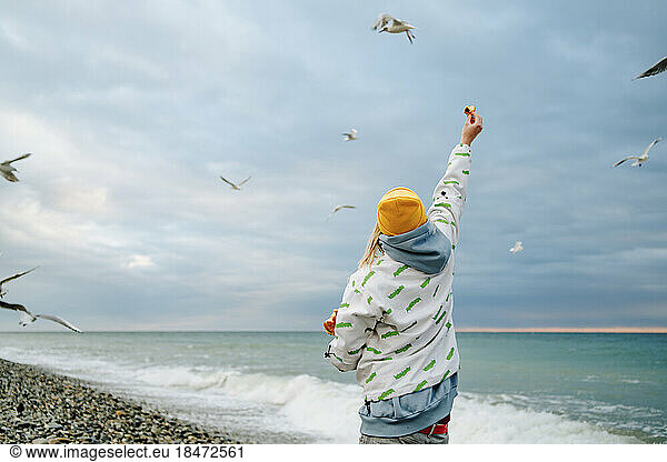 Woman with hand raised feeding seagulls at shore