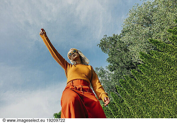 Woman with hand raised standing in garden