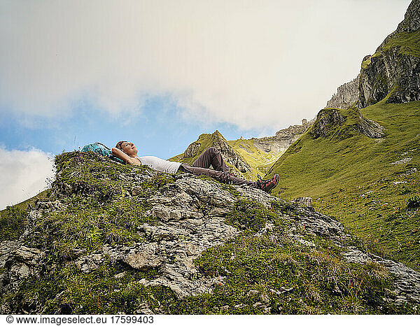 Woman with hands behind head lying on rock