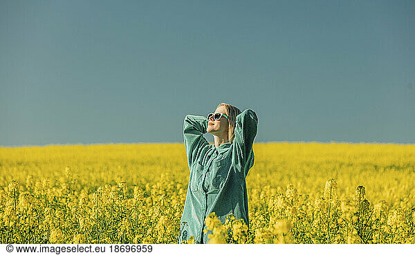 Woman with hands behind head standing in rapeseed field