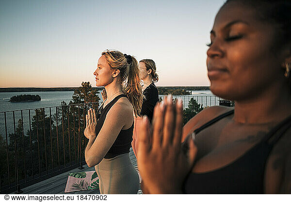 Woman with hands clasped exercising with female friends at patio