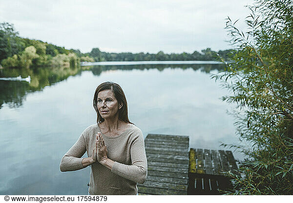 Woman with hands clasped standing on jetty by lake