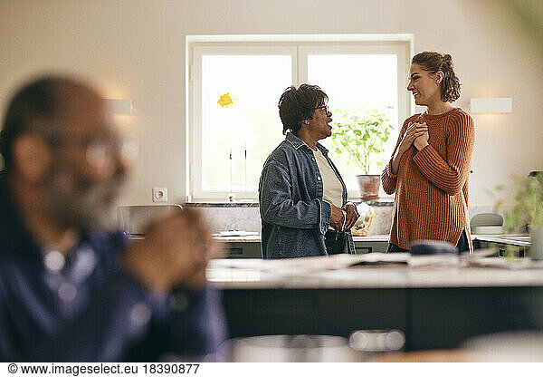 Woman with hands on chest talking to mother-in-law standing in kitchen at home