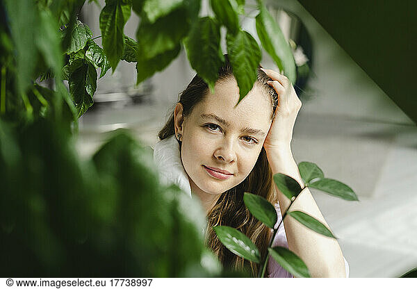 Woman with head in hand seen through plants at home