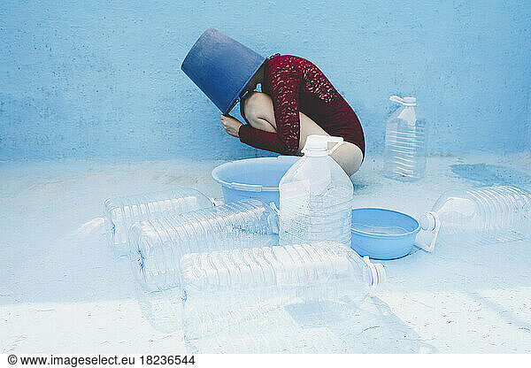 Woman with head inside bucket by plastic bottles in empty swimming pool