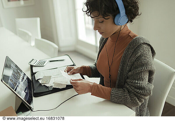 Woman with headphones and receipts paying bills at digital tablet