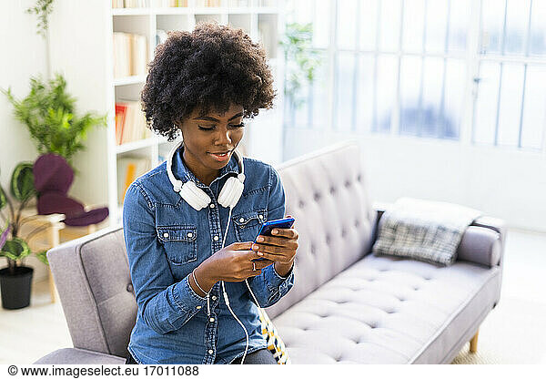 Woman with headphones using mobile phone while sitting on sofa at home