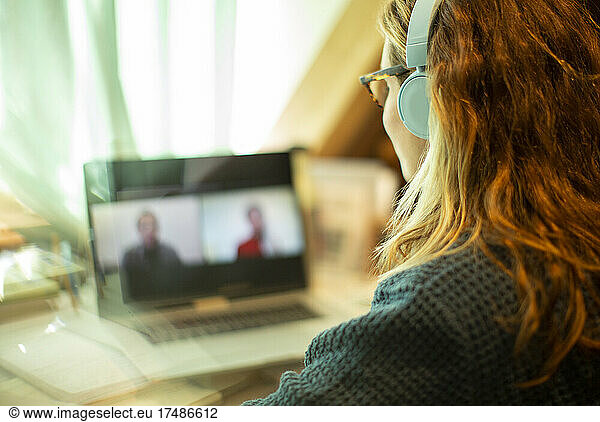Woman with headphones video chatting with colleagues at laptop