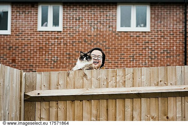 Woman with her cat smiling over garden fence saying hello to neighbour