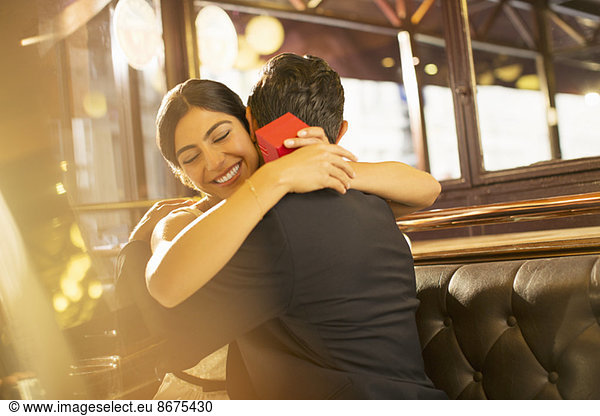 Woman with jewelry box hugging man in restaurant