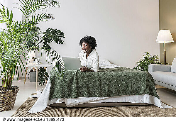 Woman with laptop lying on bed at home