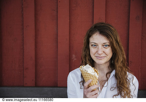 Woman with long brown hair sitting on a bench  eating ice cream.