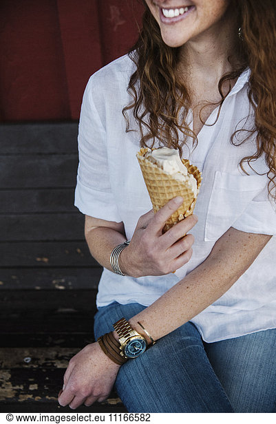 Woman with long brown hair sitting on a bench  eating ice cream.