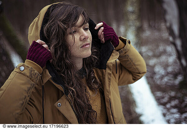 woman with long curly hair and freckles takes off hood in snow woods