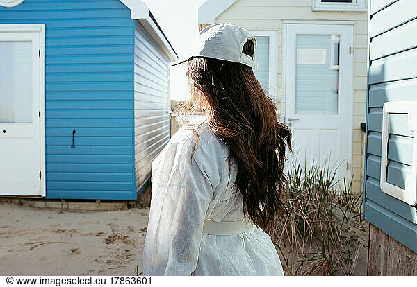 woman with long dark hair stood by beach huts by the coast in summer