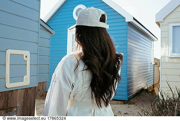 woman with long dark hair stood by colourful beach huts by the coast