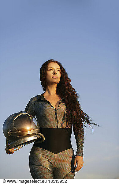 Woman with long hair holding space helmet under blue sky