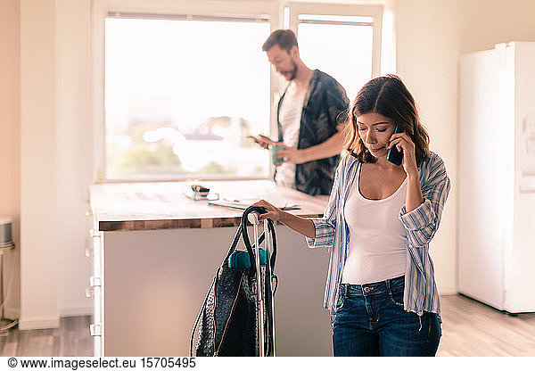 Woman with luggage talking on smart phone while man standing in background at apartment