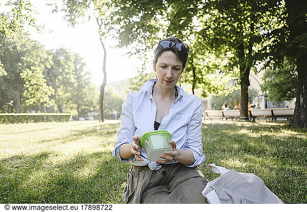 Woman with lunch box sitting in park on sunny day