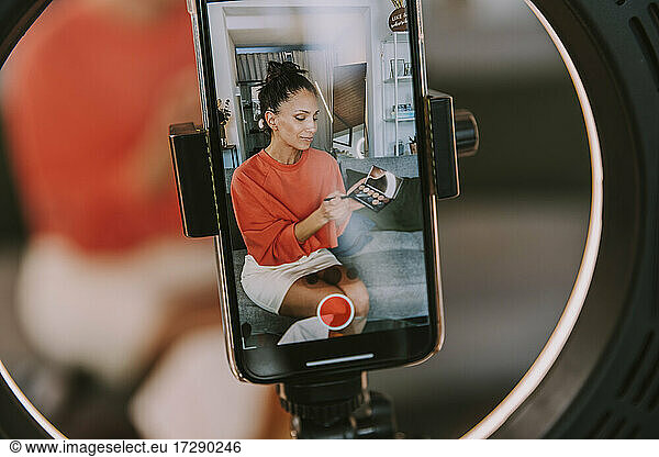 Woman with make-up palatte doing tutorial through smart phone at home
