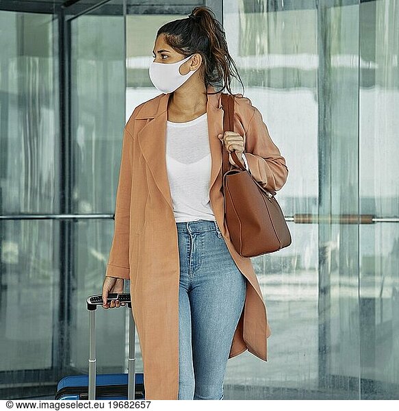Woman with medical mask carrying luggage airport during pandemic