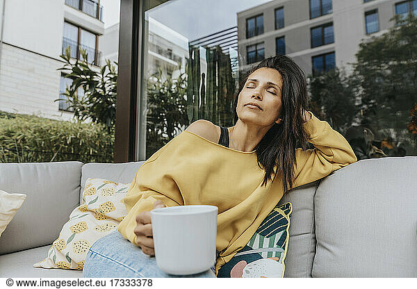 Woman with mug relaxing on sofa at backyard