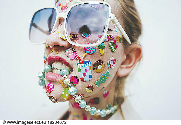 Woman with multi colored stickers on face biting necklace in front of white background