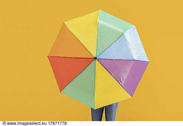 Woman with multi colored umbrella in front of yellow wall