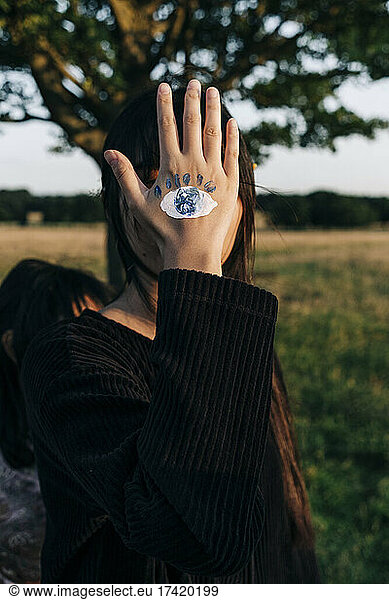 Woman with paint on hand standing covering face at park