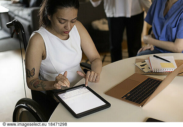 Woman with paraplegia using digital tablet by laptop on dining table at home