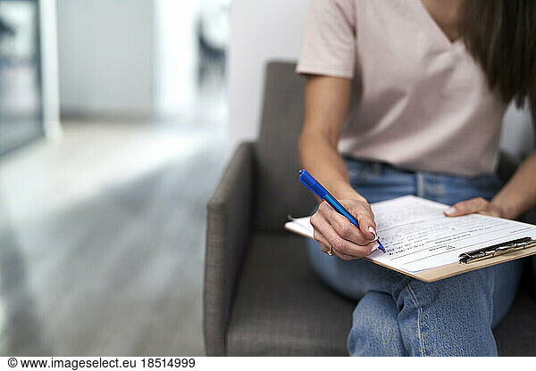 Woman with pen filling form sitting in waiting room