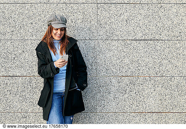 Woman with phone and casual clothes leaning against a wall