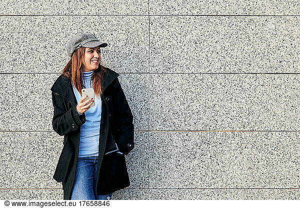 Woman with phone and casual clothes leaning against a wall