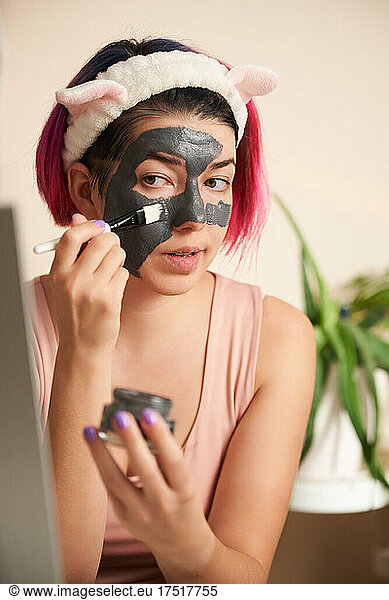 Woman with pink hair inflicts face mask of therapeutic clay.