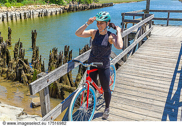Woman with Ponytail Adjusts Bike Helmet on Dock Near Water