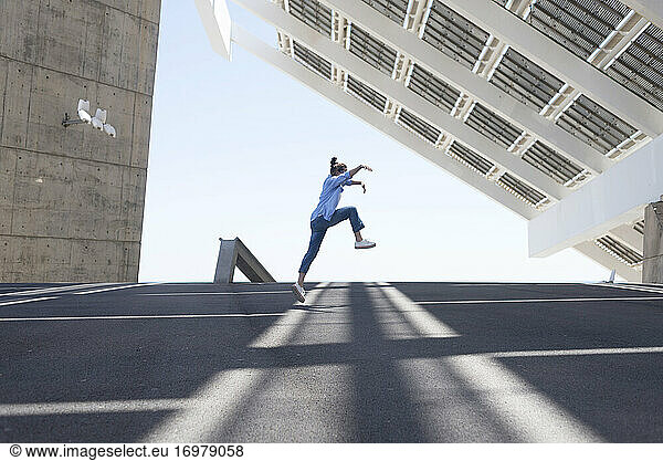 Woman with ponytail jumping in joy and raising arms in urban outside