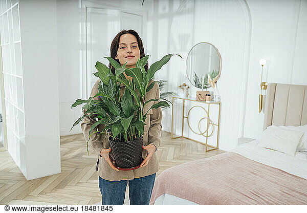 Woman with potted plant standing in bedroom at home