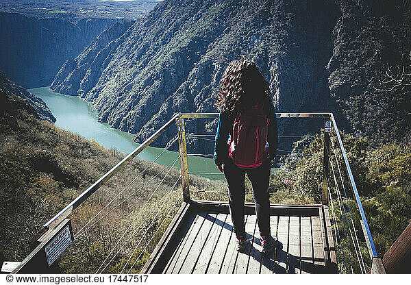 Woman with red backpack and curly hair observing the landscape up high