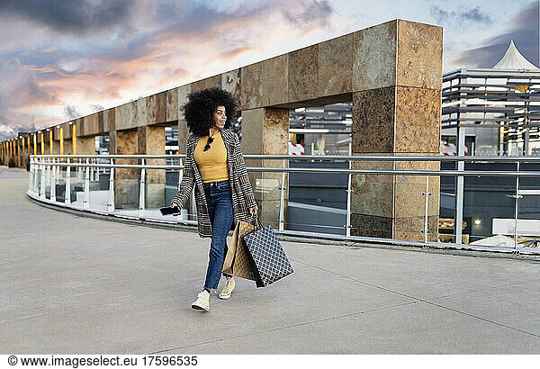 Woman with shopping bags walking on footpath at sunset