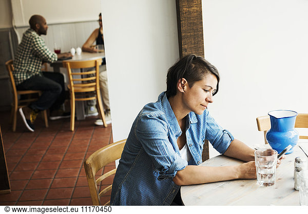 Woman with short brown hair sitting in a cafe  using a mobile phone.