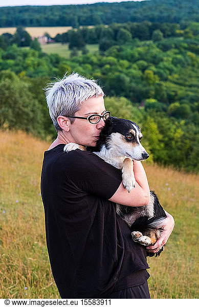 Woman with short grey hair wearing glasses standing on a hillside  holding dog.