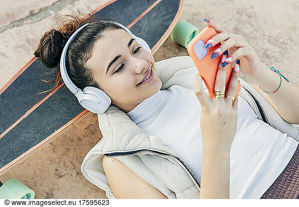 Woman with skateboard listening music on headphones and using smart phone